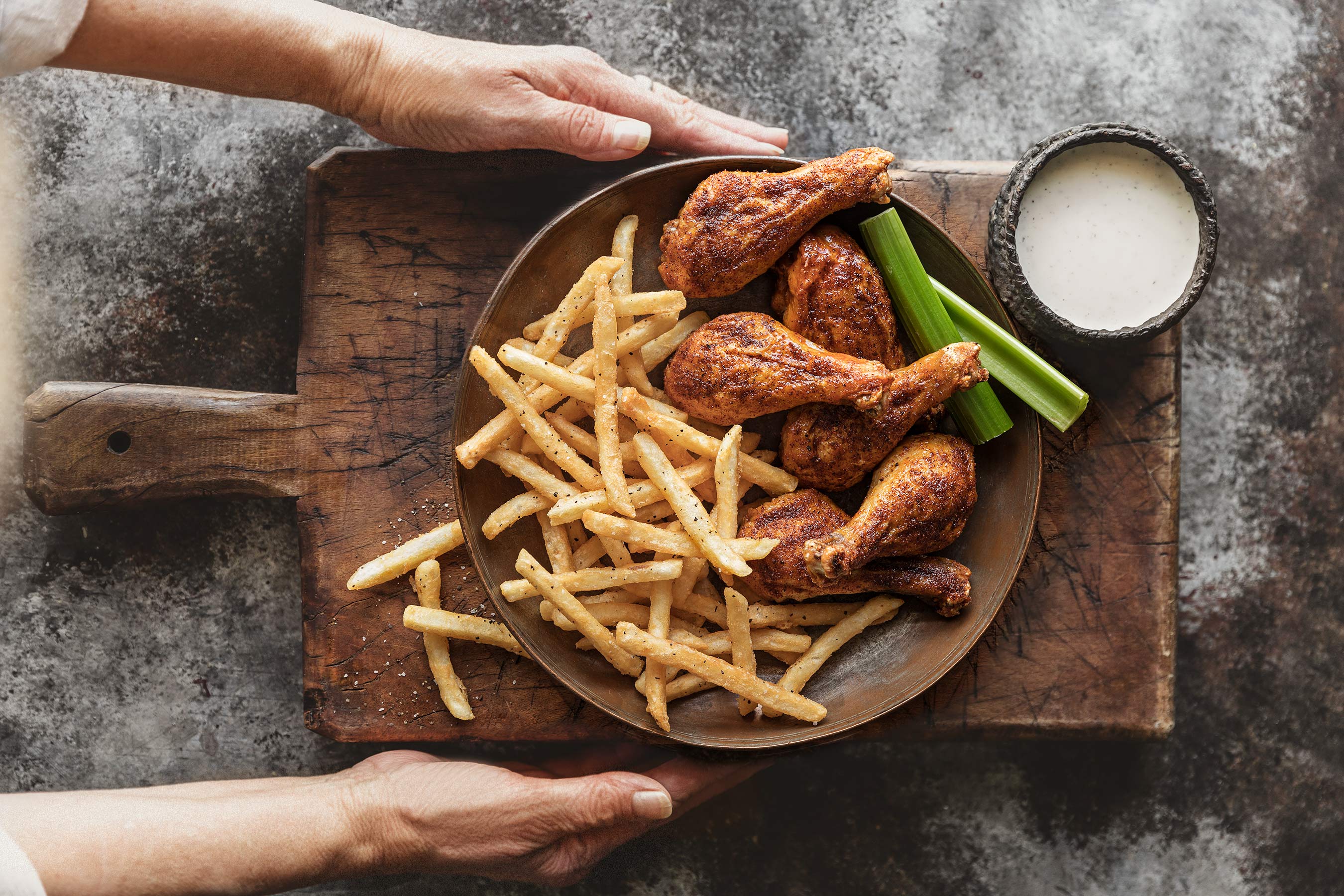 Glanger Photography | Drumsticks and Fries with celery and ranch.  Hands serving it on a wood board