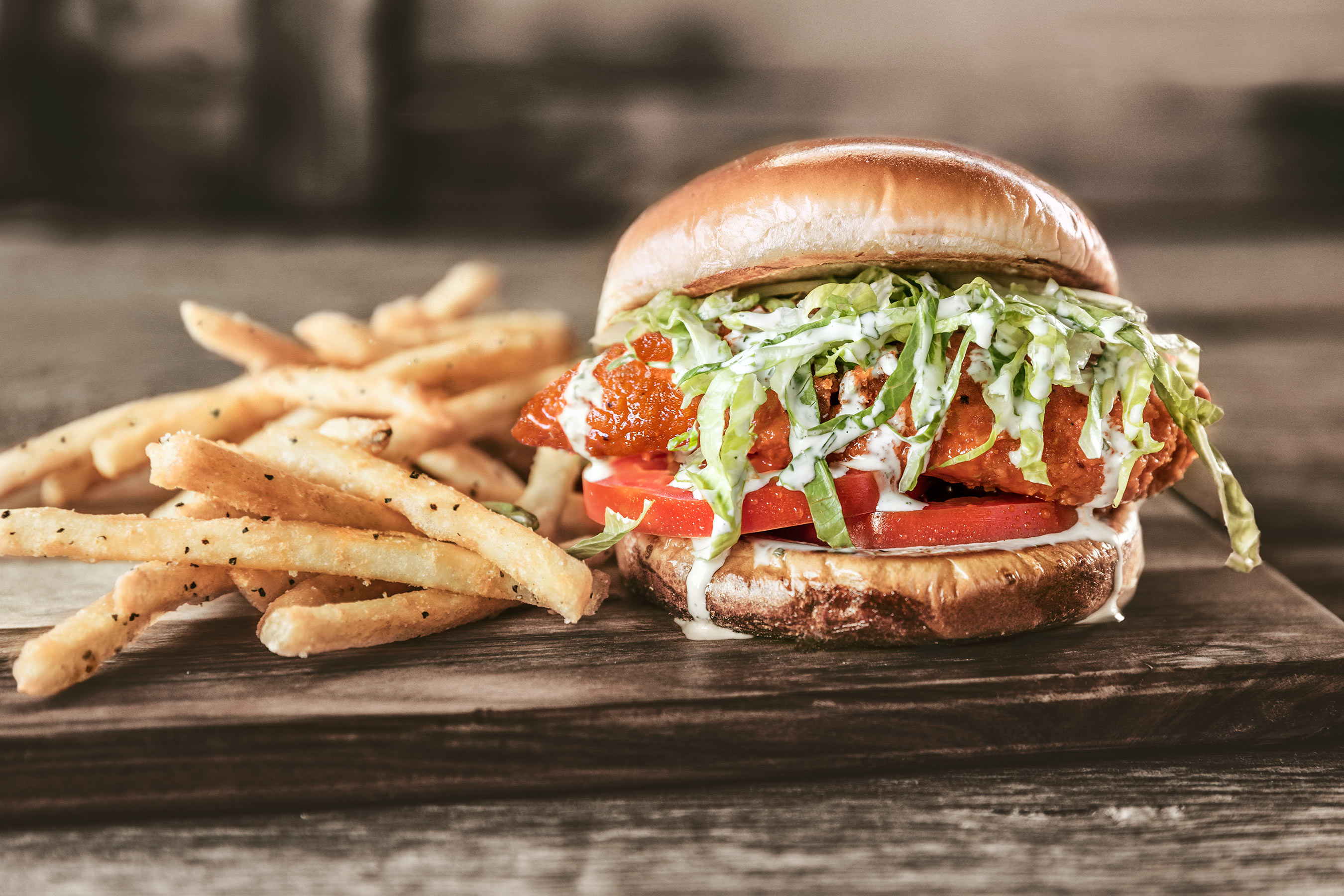 Spicy Buffalo Chicken Sandwich and Fries on rustic wood surface