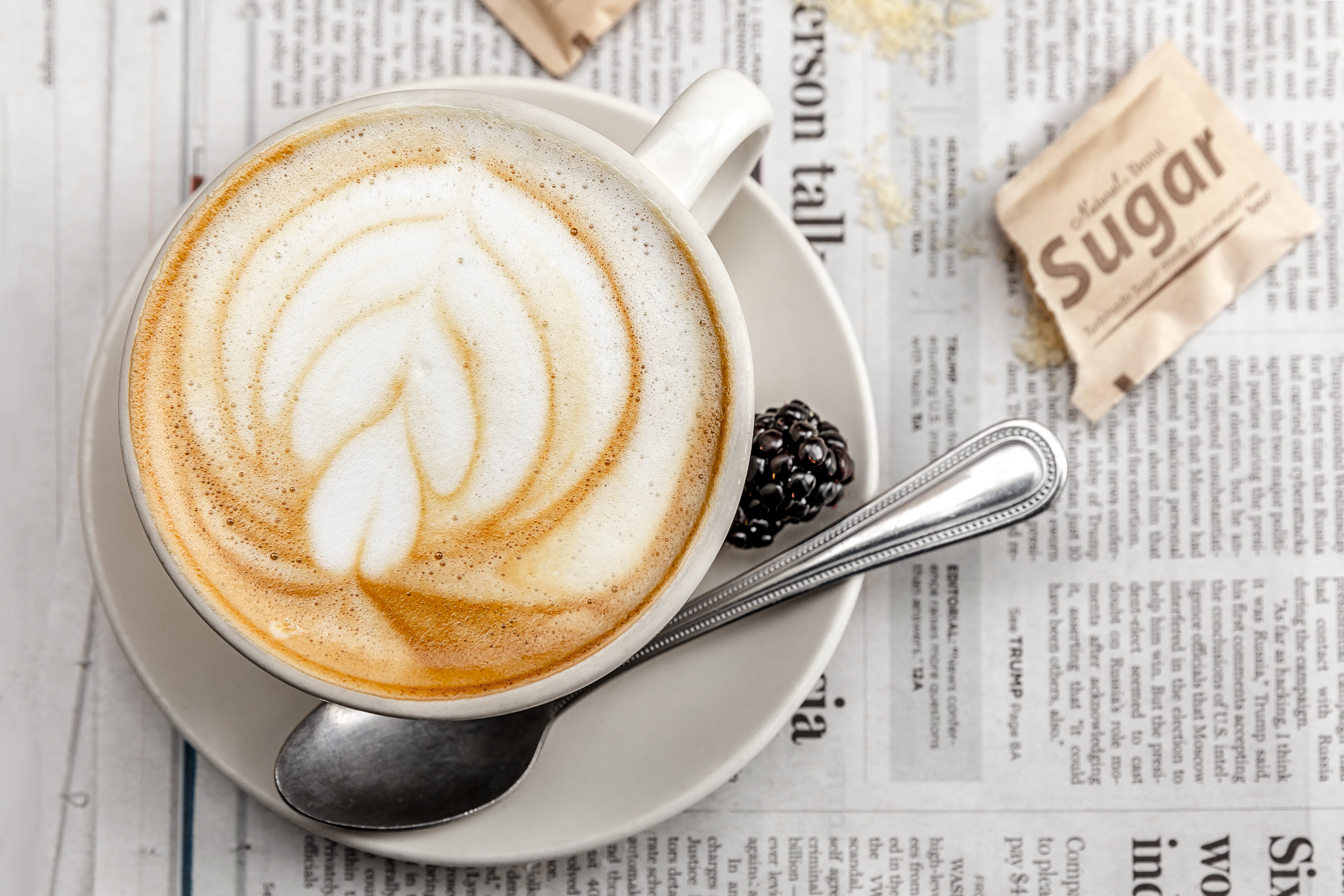 Glanger Photography | Coffee with swirl design in the foam.  On a newspaper with sugar packet nearby