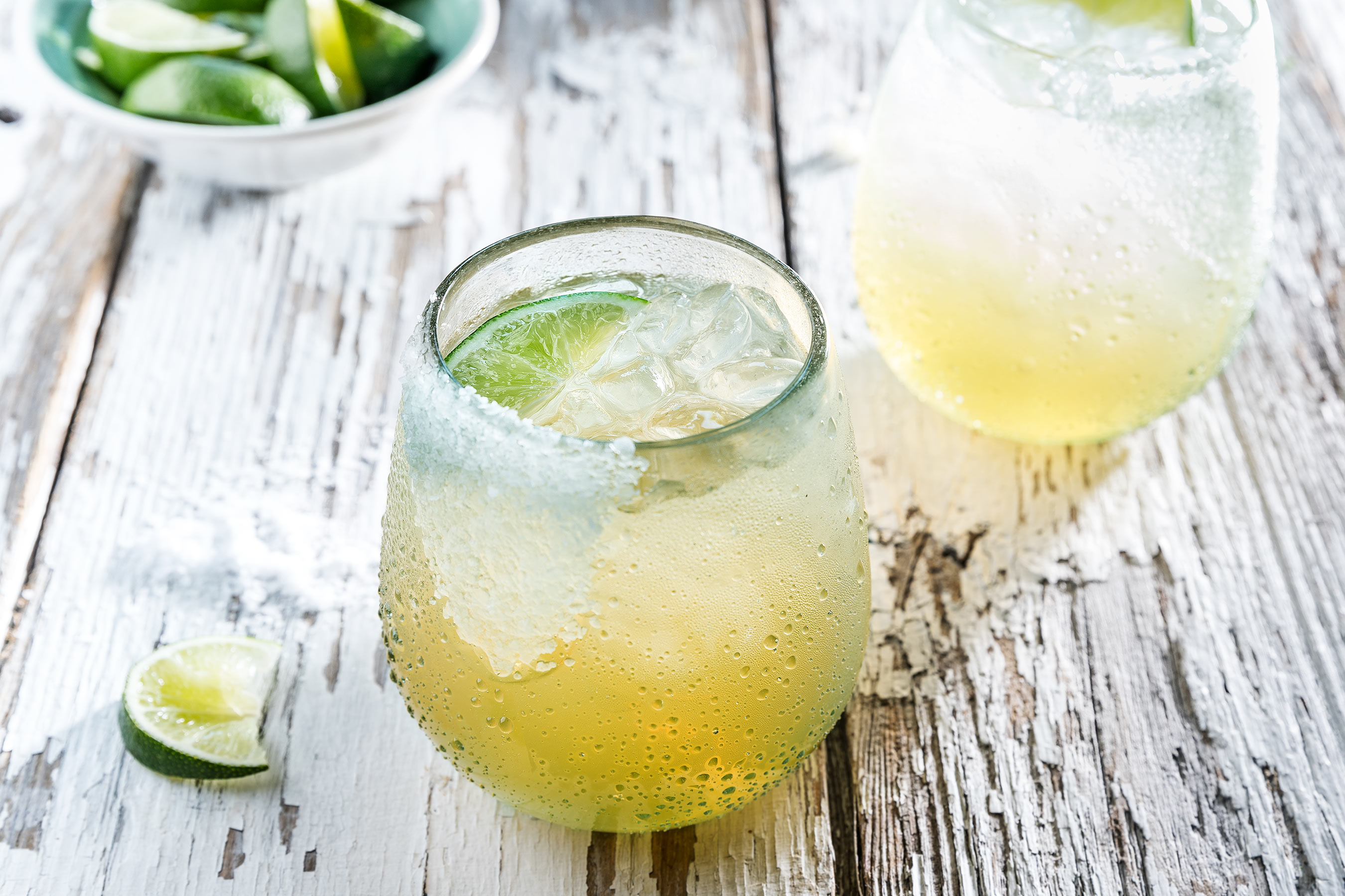 Margaritas on the rocks with limes on a rustic white surface