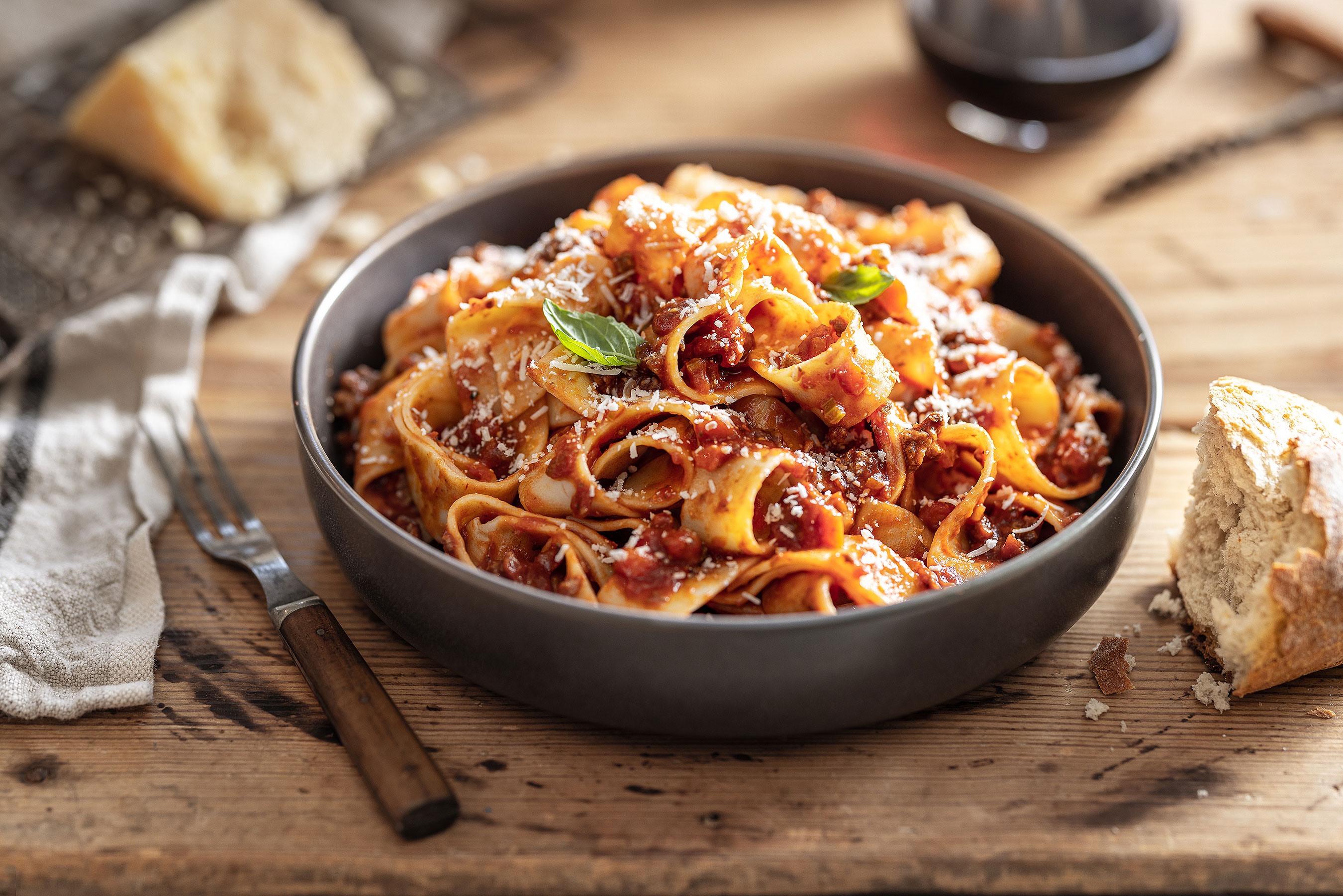 Glanger Photography | Rustic pasta bolognese with wide Pappardelle noodles on a wood surface with tomato marinara sauce in a low bowl. 